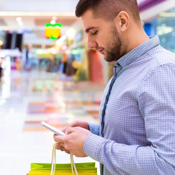 A man holding shopping bags and looking at his phone.