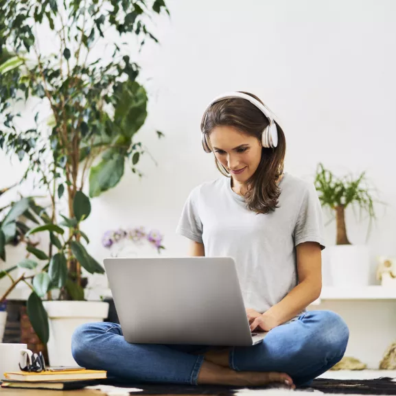 Young woman at home sitting on the floor using laptop and listening to music.