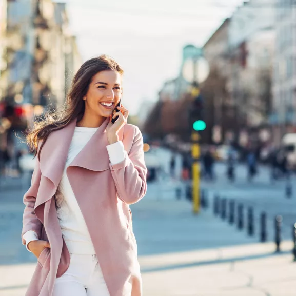 Elegant woman walking on the sidewalk at urban setting and talking on the phone.