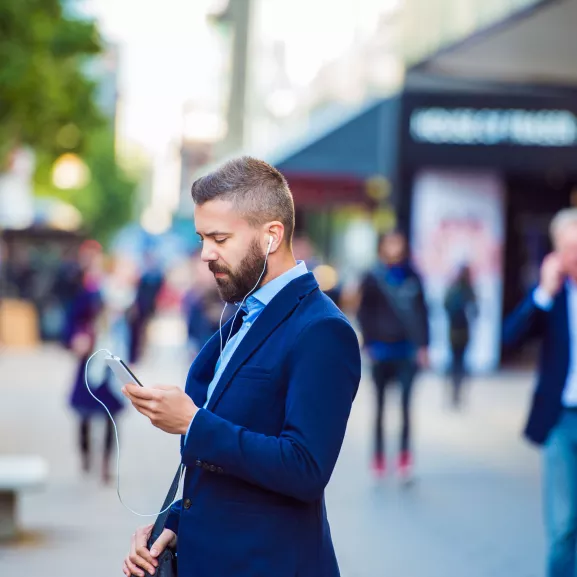 Manager with smartphone listening music outside in the street.