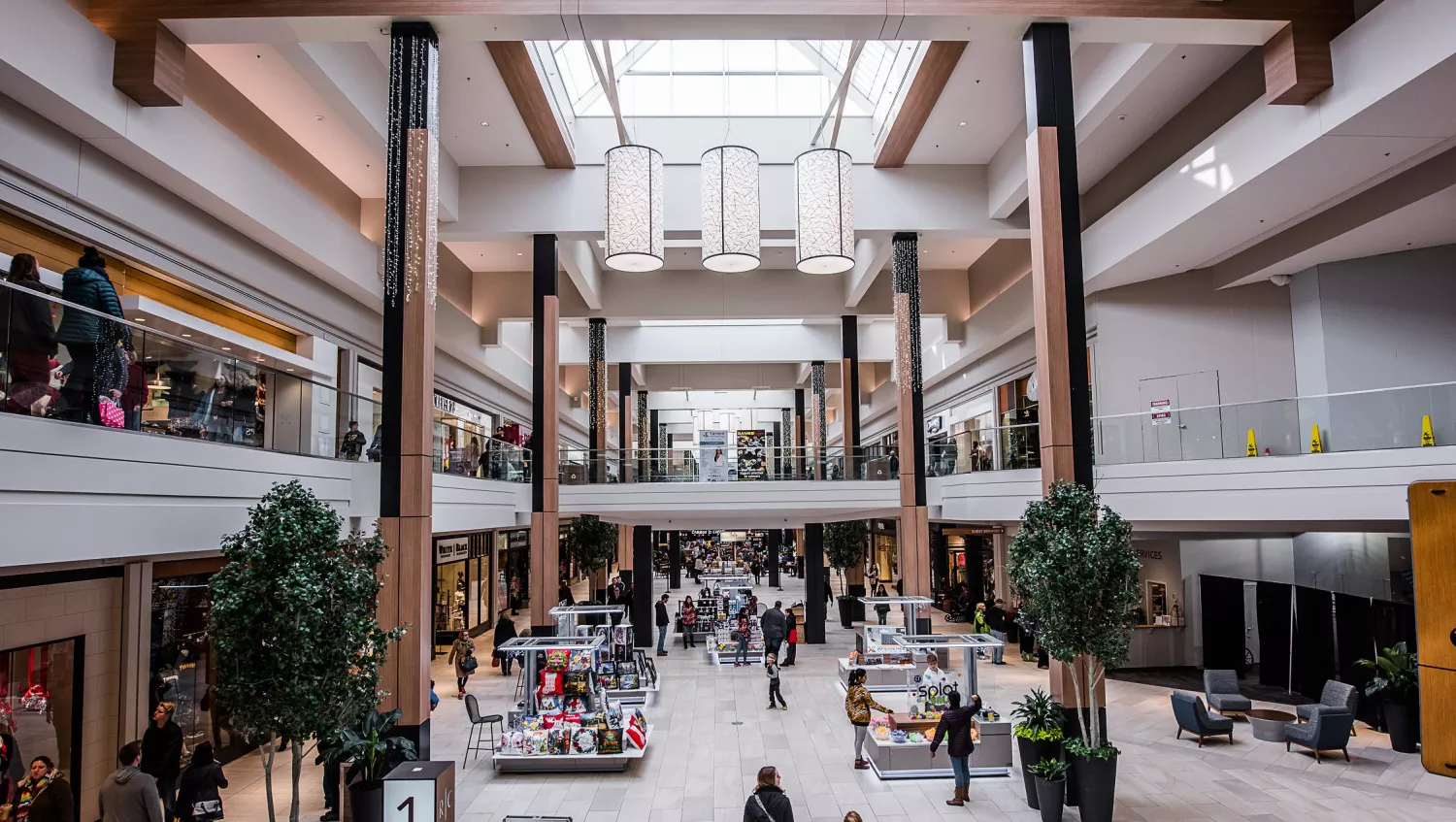 open mall with two floors, skylights creating a sunlit atmosphere, people walking in and out of stores