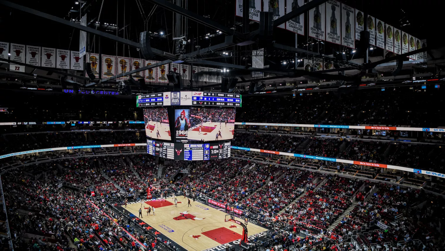 Basketball arena, with a large crowd and Jumbotron featuring the players on the court