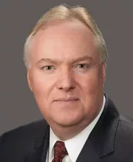 Professional headshot of a man in a suit on a dark grey background